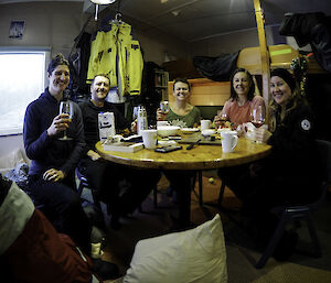 A group of people round a table, smiling to camera and holding up their glasses.