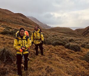 Two expeditioners, walking towards camera through grassy tussocks.