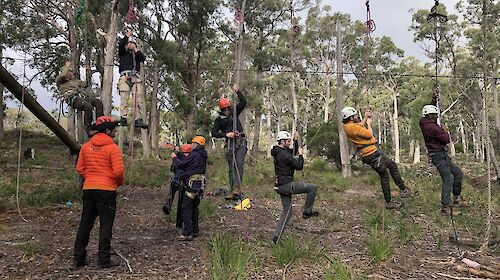 Six people embarking on a ropes course wearing hardhats.