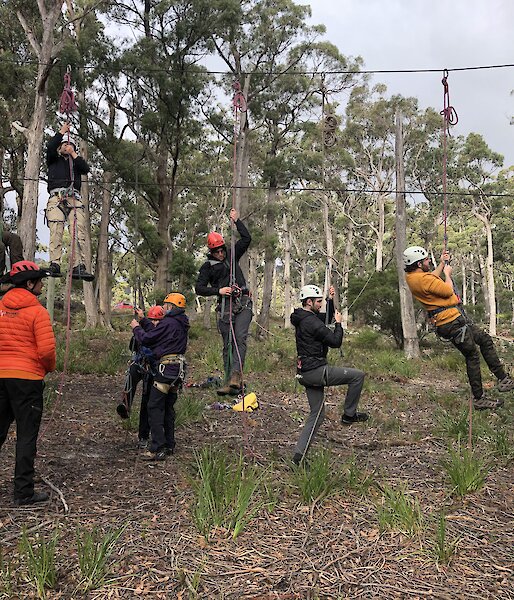 Six people embarking on a ropes course wearing hardhats.