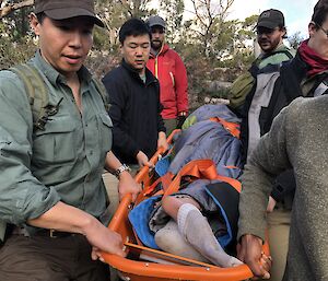 A group of people carry a mock patient on a stretcher.