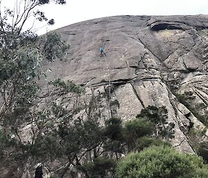 A woman scales down a rock cliff from a distance.