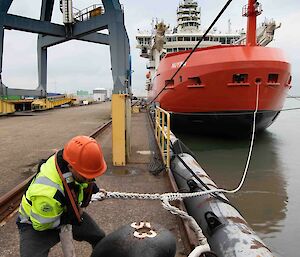 A man unties a heavy rope from the dock attached to a large ship