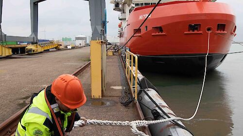 A man unties a heavy rope from the dock attached to a large ship