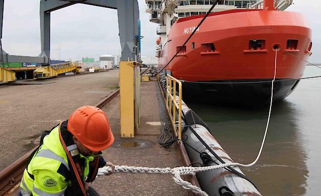 A man unties a heavy rope from the dock attached to a large ship