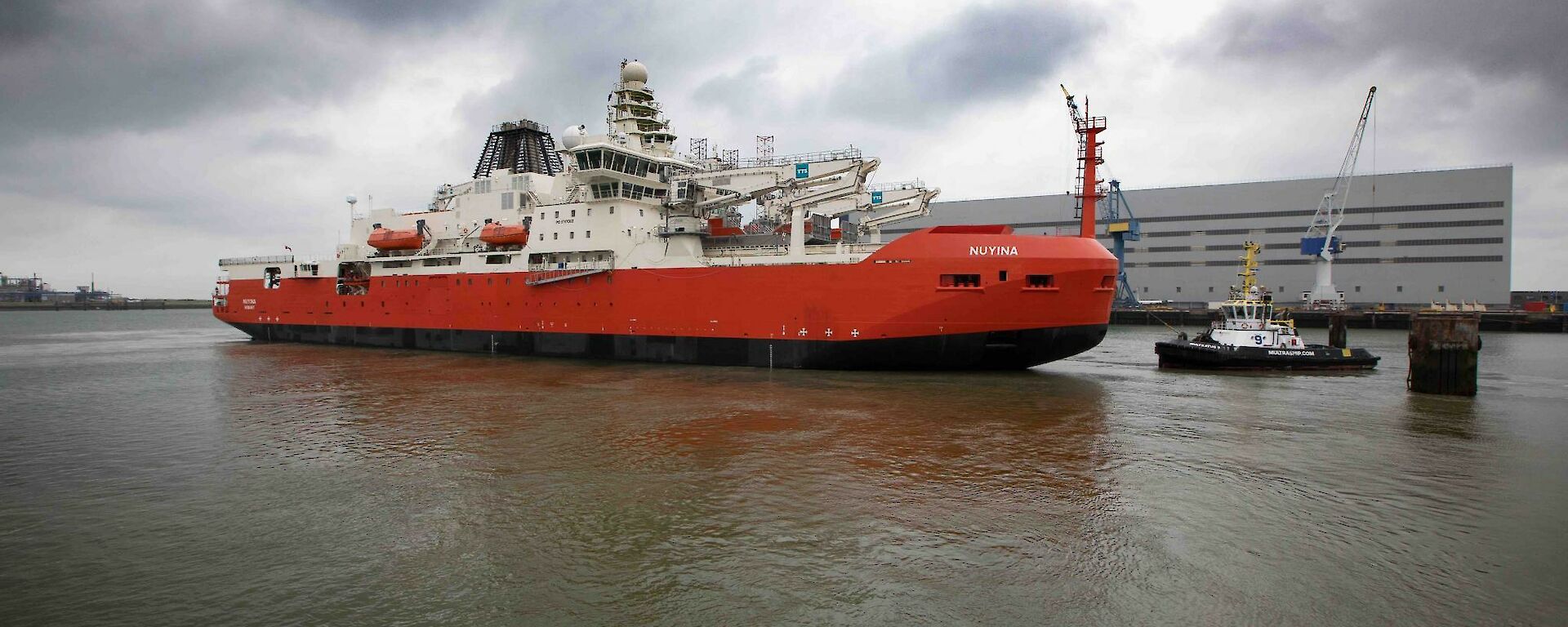 A large red ship with a tug boat beside it in dock