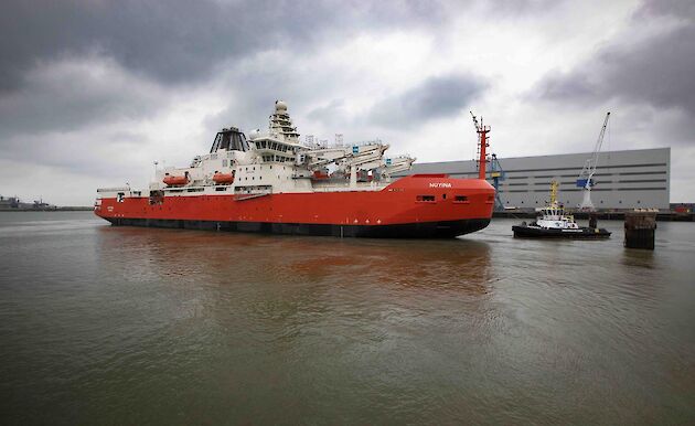 A large red ship with a tug boat beside it in dock