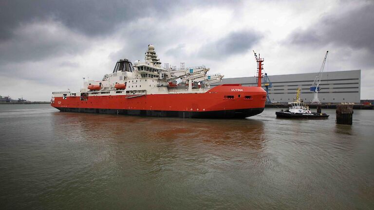 A large red ship with a tug boat beside it in dock