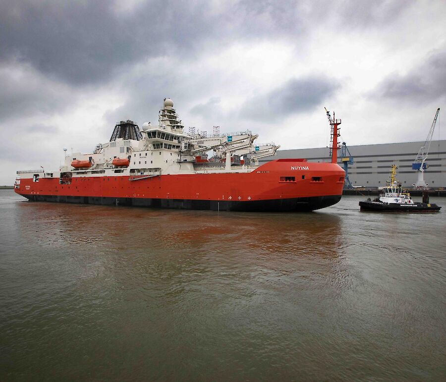 A large red ship with a tug boat beside it in dock