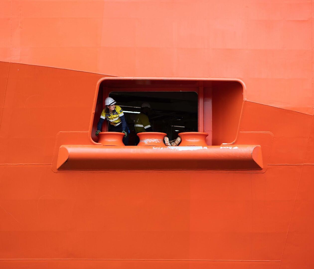 A worker in hi vis seen peeking out of port hole in the side of a ship