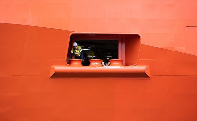 A worker in hi vis seen peeking out of port hole in the side of a ship