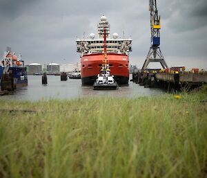 Looking across some grass towards a red ship being pulled by a tug boat