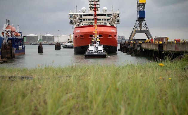 Looking across some grass towards a red ship being pulled by a tug boat