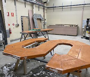 A large metal S propped up on two saw-horses in a warehouse