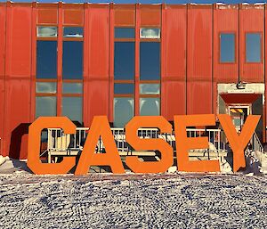Large metal letters spelling CASEY leaning up against a large red shed in the snow