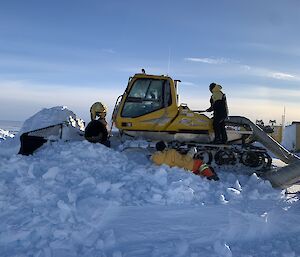 A snow bound groomer being dug out of a large pile of snow by 3 men