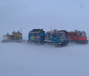 Hagglunds and sleds huddled together on the sea ice with blowing snow all around