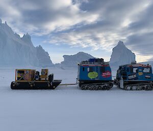 Blue Hagglund and sled pass on the sea ice with magnificent icebergs in the background