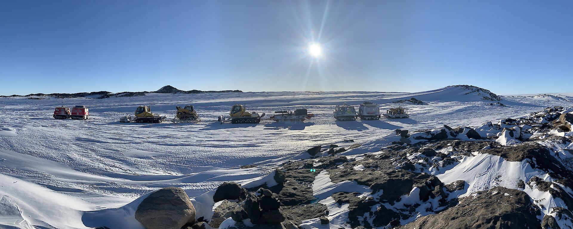 A panoramic shot across an icy Antarctic landscape with a convoy of vehicles traversing across the snow