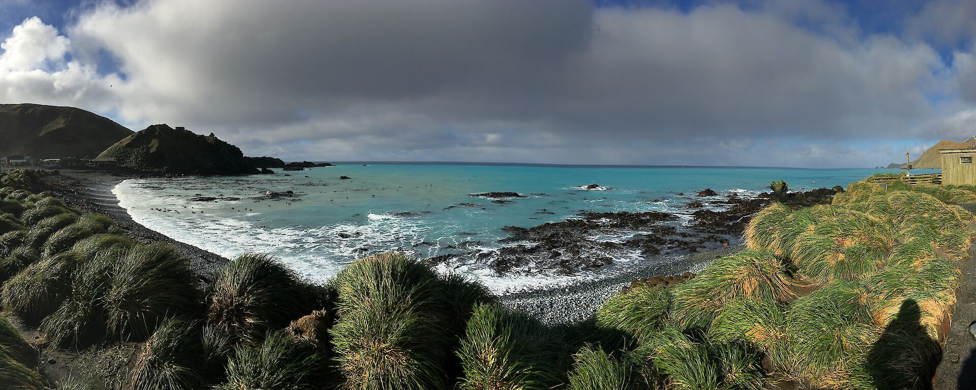 Blue seas fill a bay surrounded by a rugged green foreshore