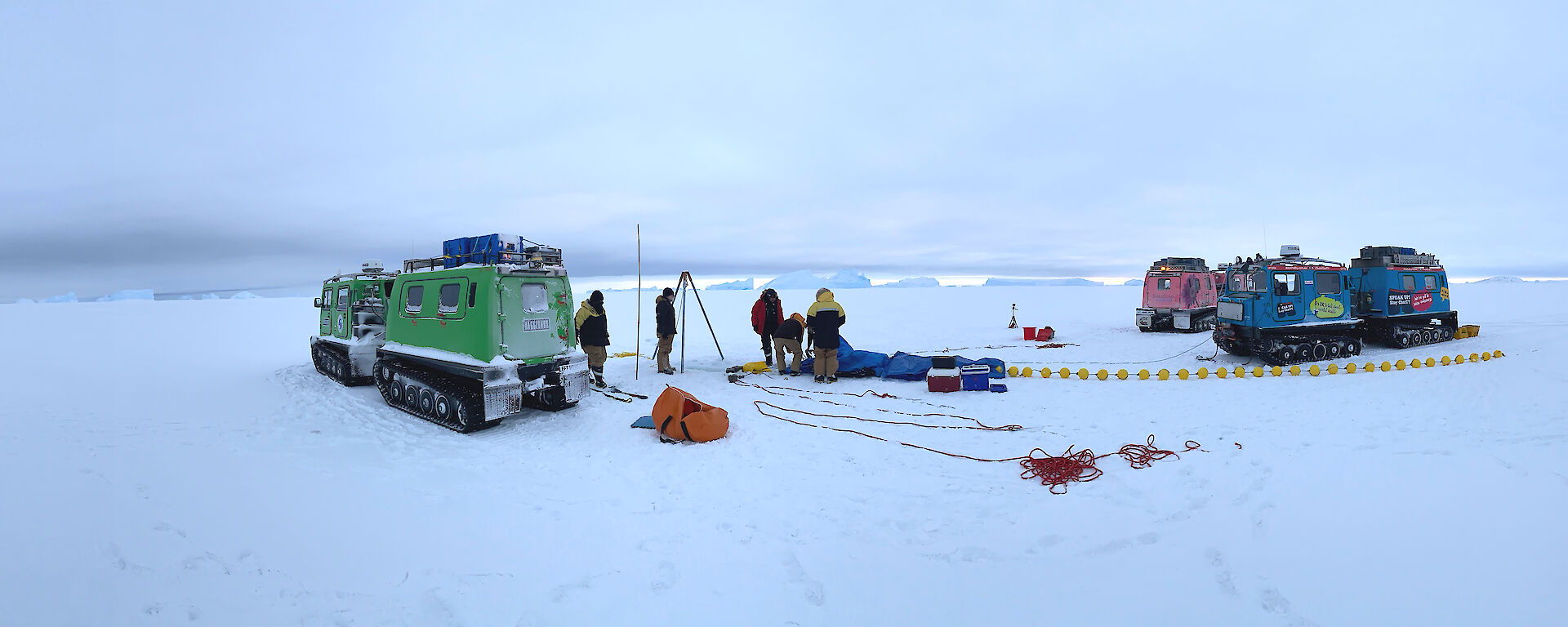 Two hagglunds and scientists gathered on sea ice, with scientific instruments.