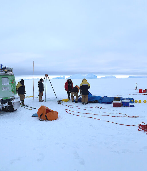 Two hagglunds and scientists gathered on sea ice, with scientific instruments.