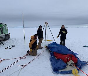 Three scientists preparing to deploy a scientific instrument through a hole in sea ice.