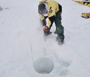 Expeditioner cutting a hole in sea ice with a chainsaw.