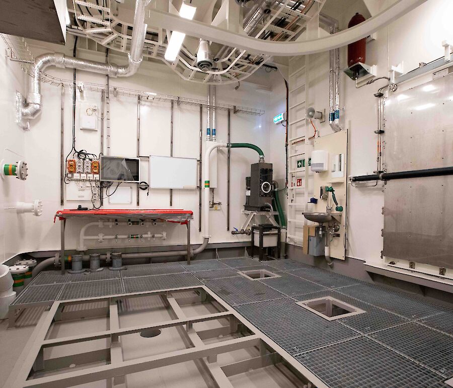 A small empty room with a grated floor and pipework on the walls.