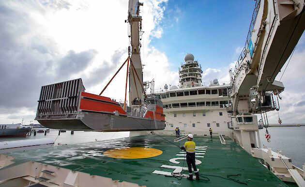 A barge being craned onto the bow of the ship with one of its 50 tonne cranes.