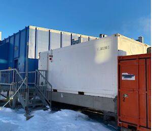 A group of coloured sheds in the snow.  A metal walkway leading to the door.