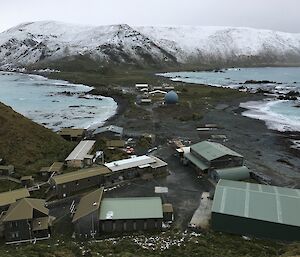 Looking downhill towards a collection of buildings on an isthmus.  Snow capped mountains sit on the far side