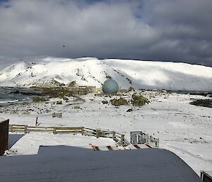 A snowy landscape with some buildings, fencework and round communications building