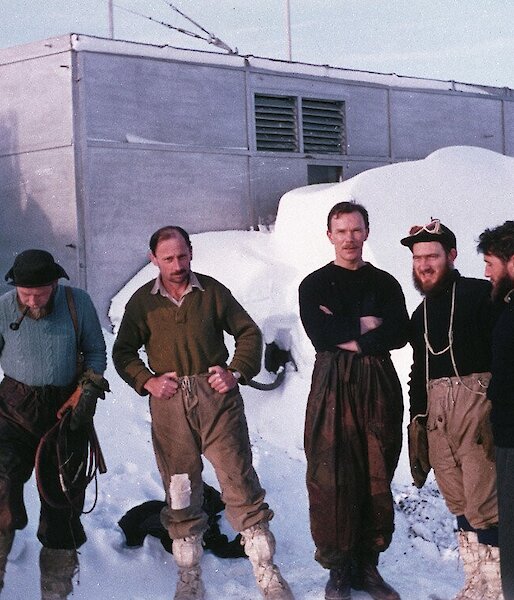 5 men stand in the snow in front of an original building - the first Davis station wintering party in 1957