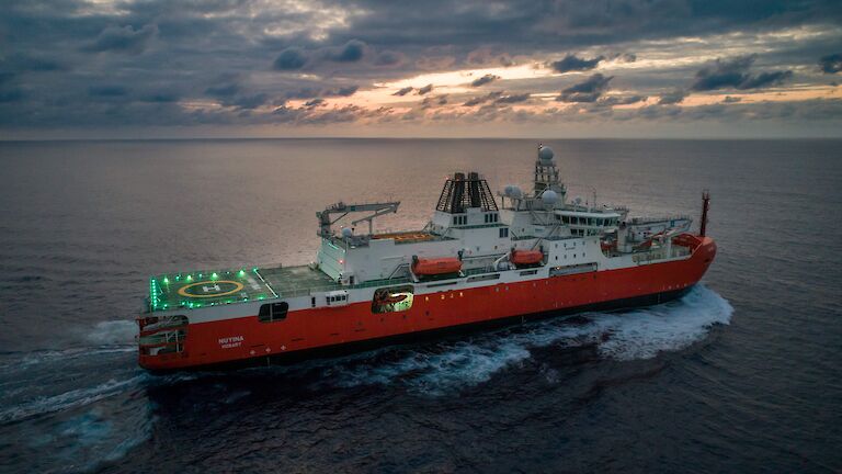 RSV Nuyina in the Atlantic Ocean at sunrise with lights illuminating the helideck.