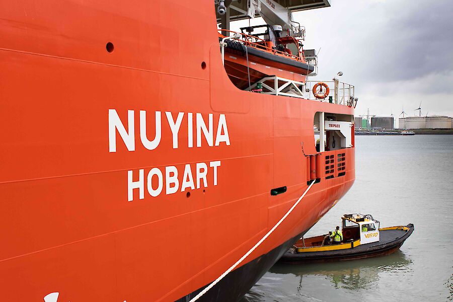 The rear of a large red and white ship with Nuyina Hobart.  A small dinghy is seen just in front.