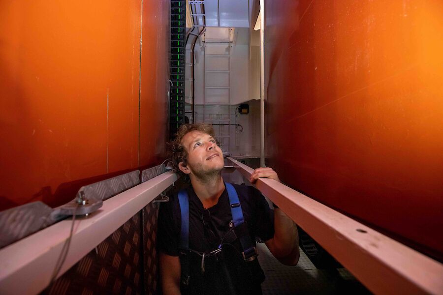 A man stands in a narrow passageway between two large orange keels