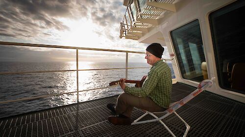 A man plays a guitar on the deck of a ship
