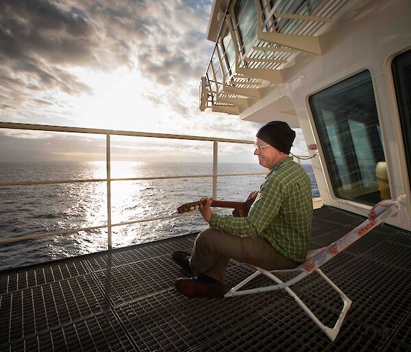 A man plays a guitar on the deck of a ship