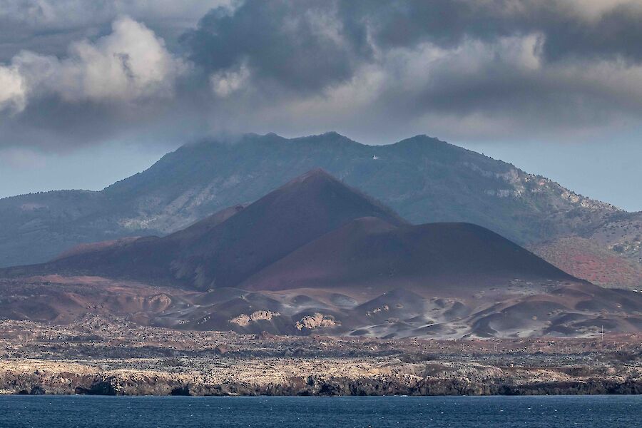 A view from the ship of a mountainous island coloured red from the volcanic soil
