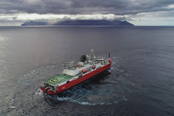 Large red ship turning in front of a cloud covered island