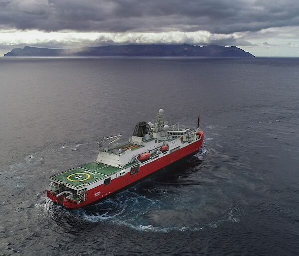 Large red ship turning in front of a cloud covered island