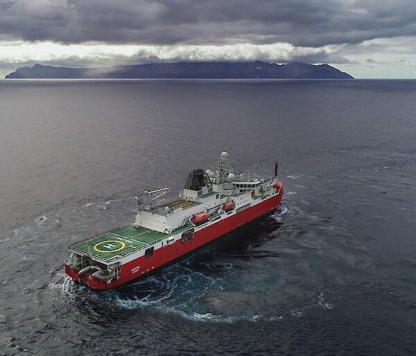 Large red ship turning in front of a cloud covered island