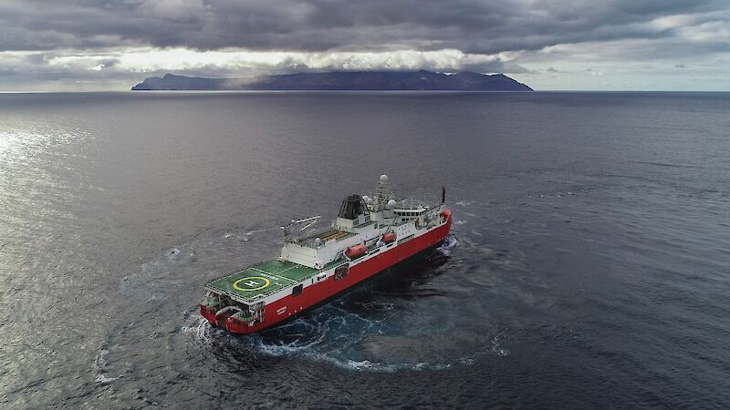 Large red ship turning in front of a cloud covered island