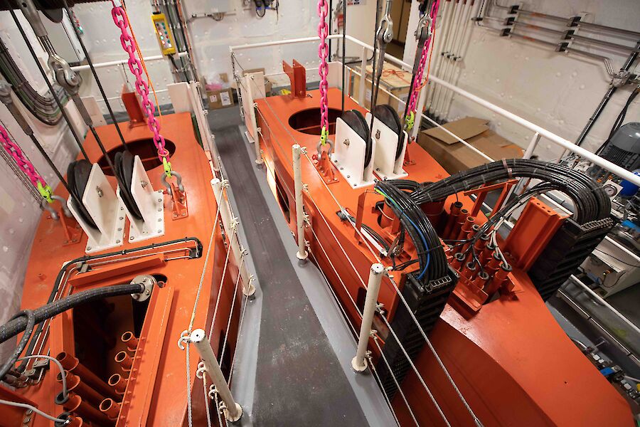 Two orange metal drop keels inside a ship suspended by winch cables