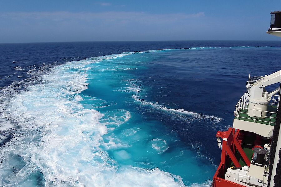 Looking out the side of a ship towards the wake caused by turning which has made the water turquoise