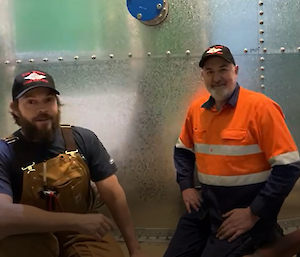 Two men, one in hi-vis in front of the new galvanised water tank.