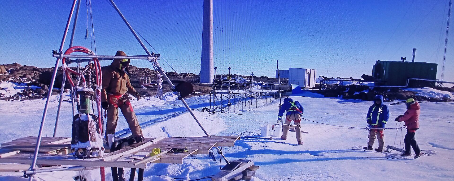 Expeditioners working on the melt bell with a large tripod to support the equipment.