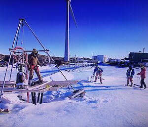 Expeditioners working on the melt bell with a large tripod to support the equipment.