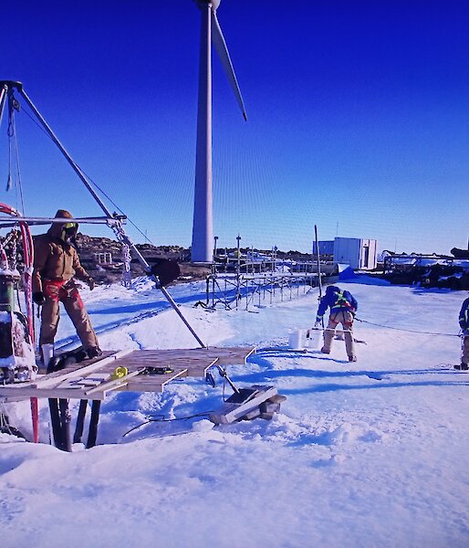 Expeditioners working on the melt bell with a large tripod to support the equipment.